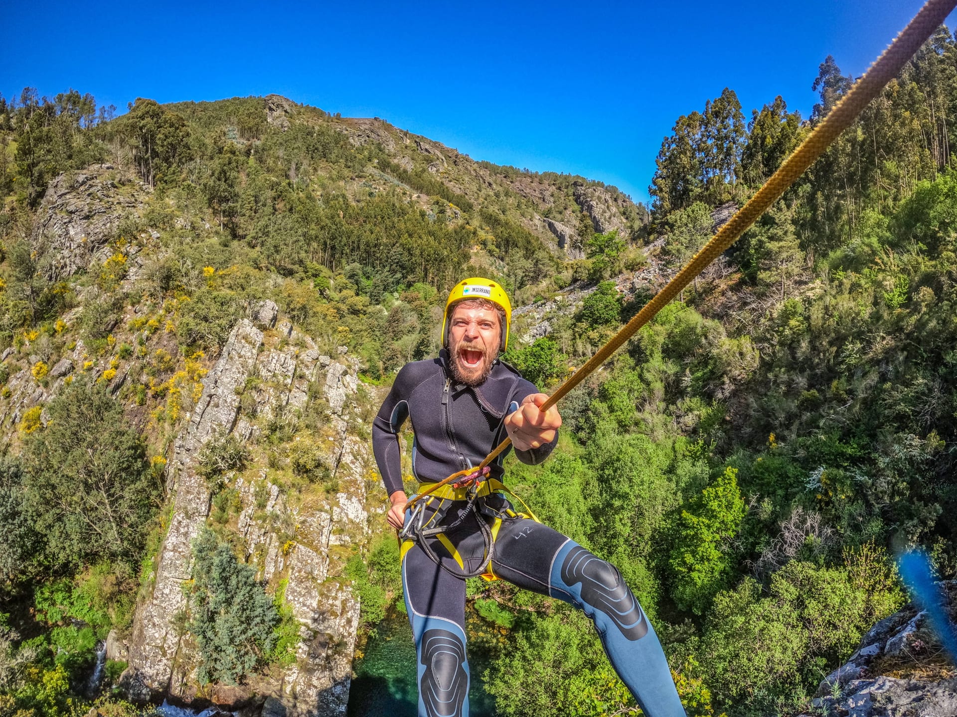 Participante de canyoning a descer por corda numa encosta rochosa