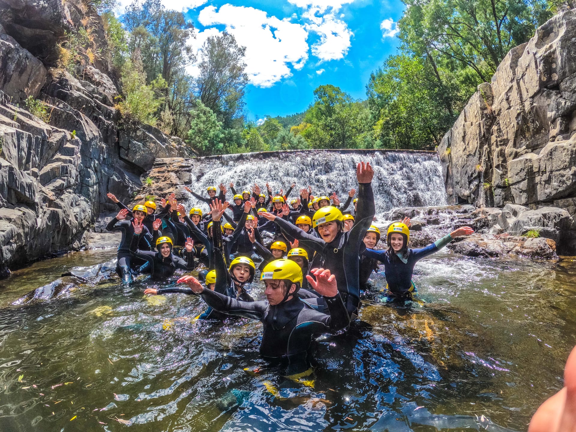 Grupo equipado numa atividade aquática diante de uma queda de água